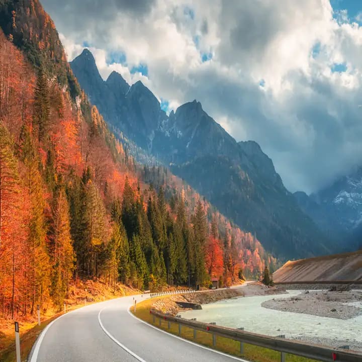 Mountain road through autumn forest under a cloudy sky